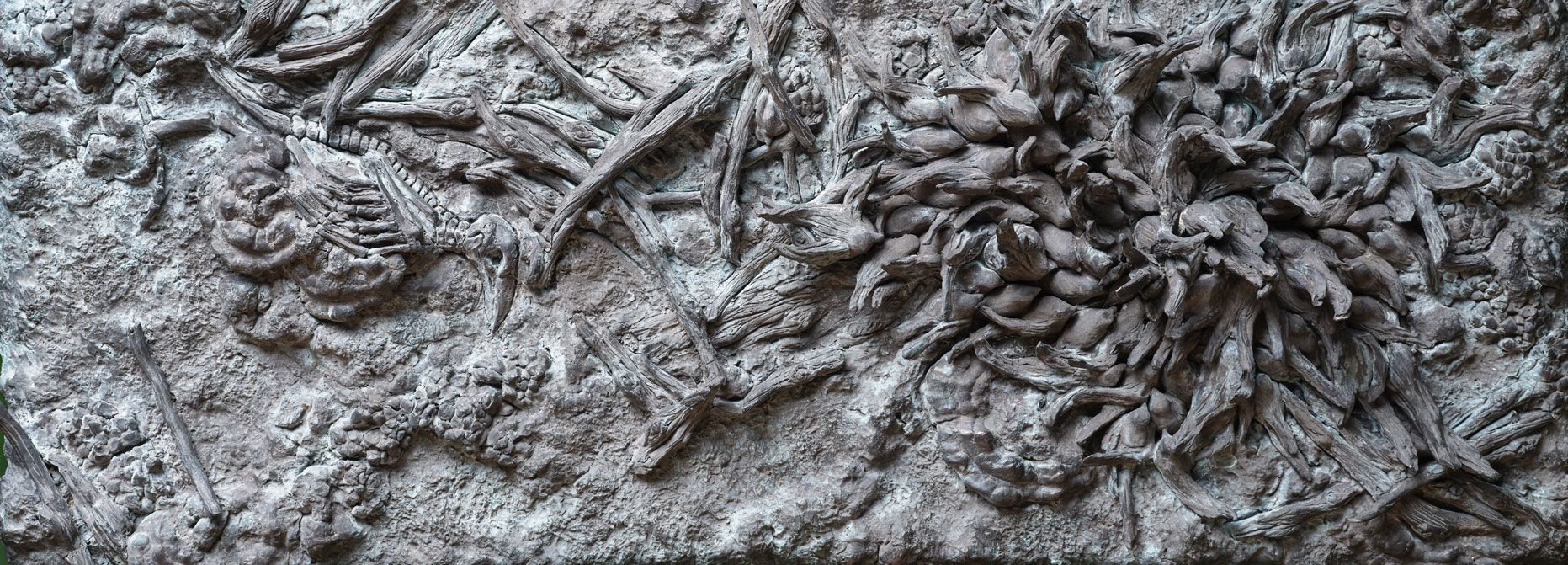 Bronzerelief med grene, kogler og organiske naturformer samlet i en tæt komposition.