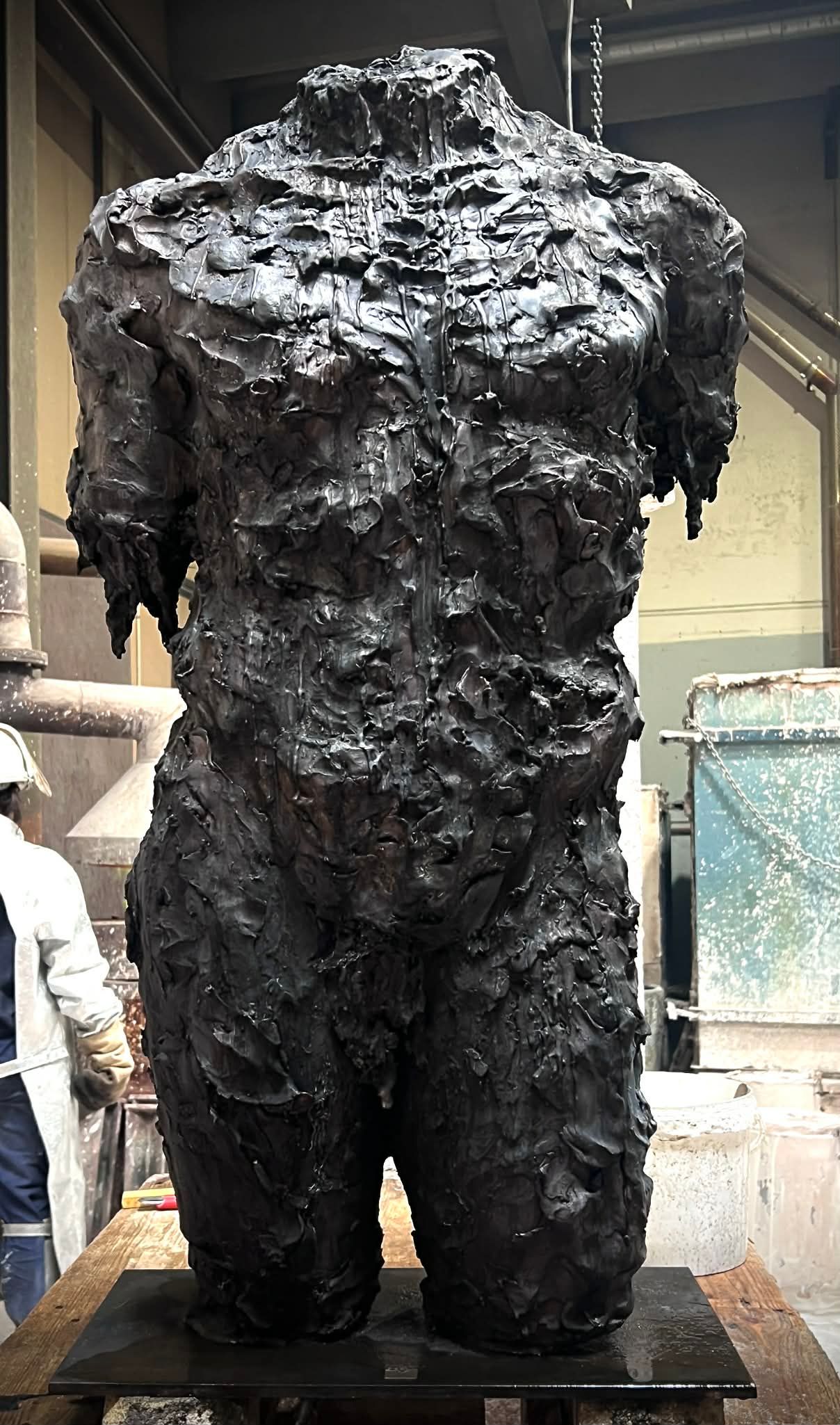 Stor bronzeskulptur af hovedløs krop med grov, dryppende overflade.