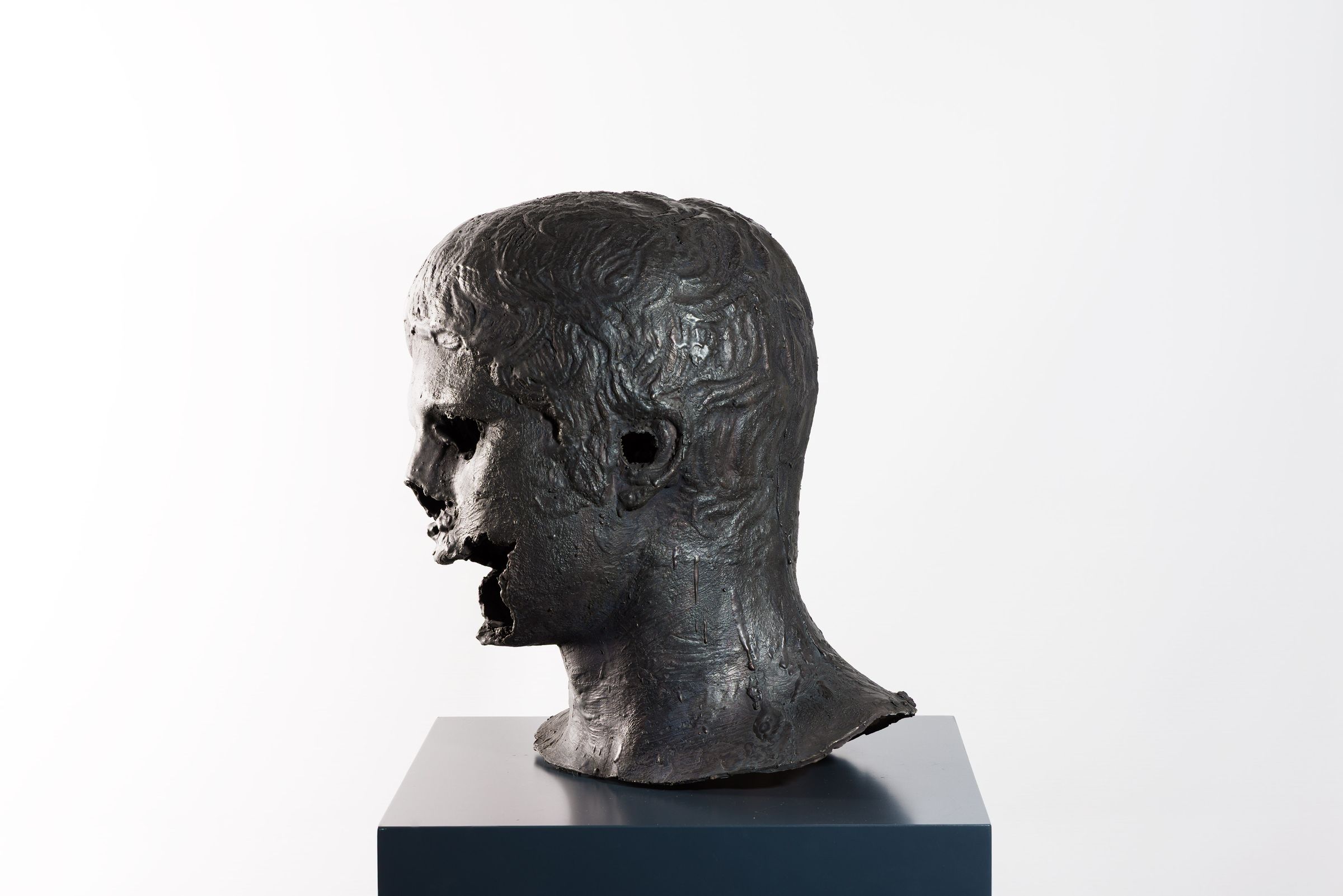 Bronze sculpture of a head with open voids in the face and rough textured surface.