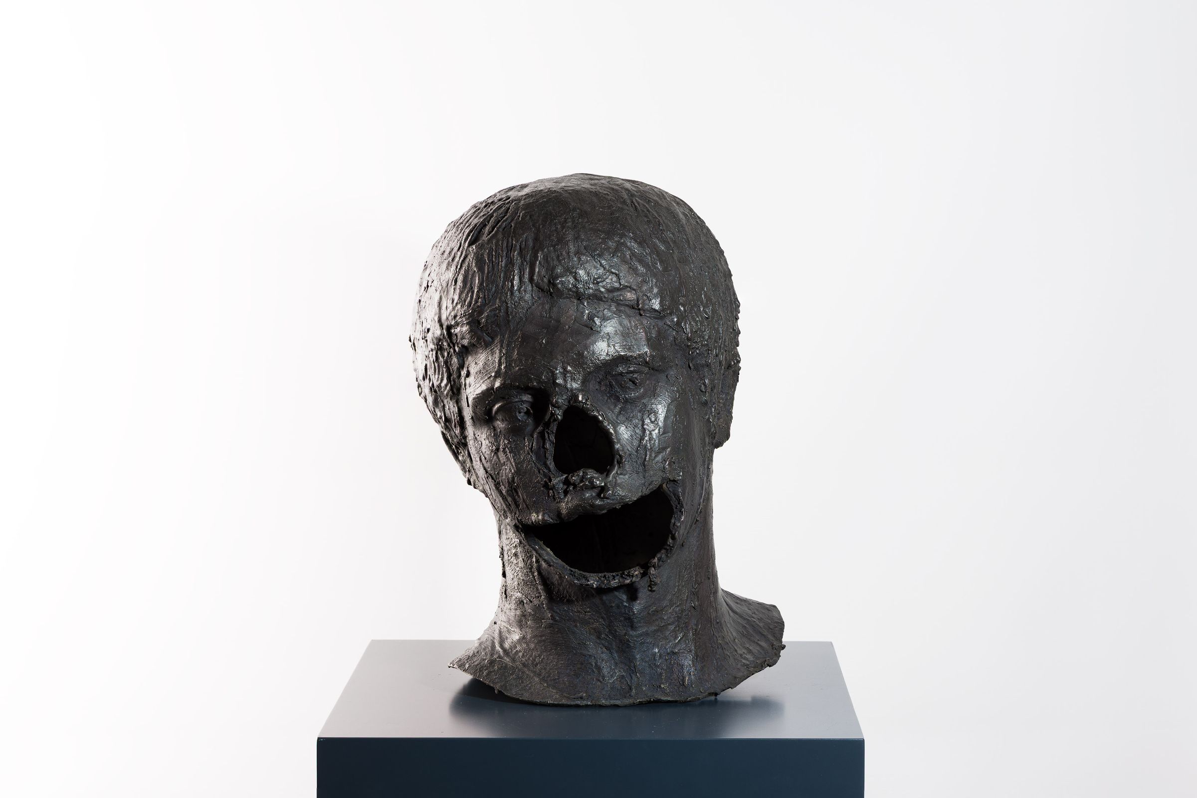 Bronze sculpture of a head with an open hole in the face and rough textured surface.