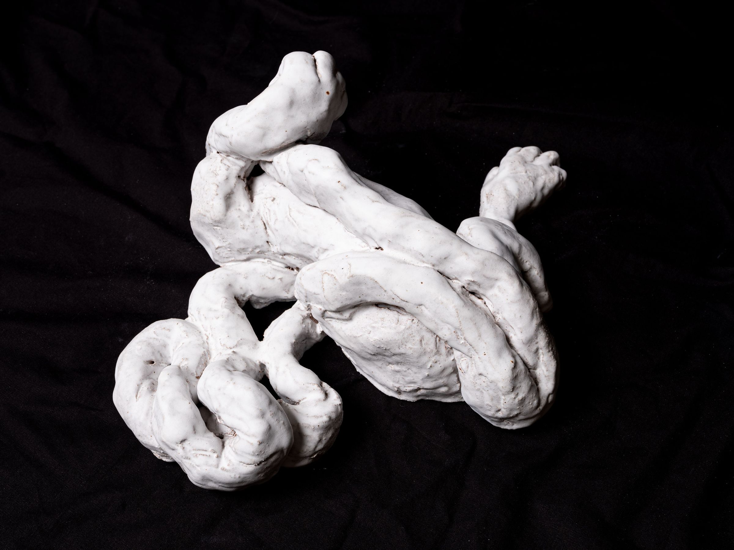 Small Misunderstandings (Lille Misforståelser), white ceramic sculpture from 2022 with intertwined organic forms set against a dark background.