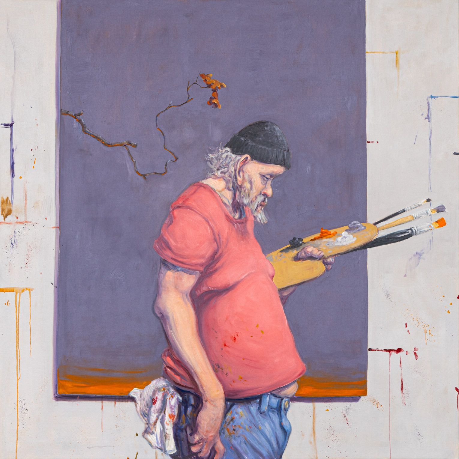 Bearded man wearing a hat holds a painter’s palette while standing in front of a canvas in a studio.