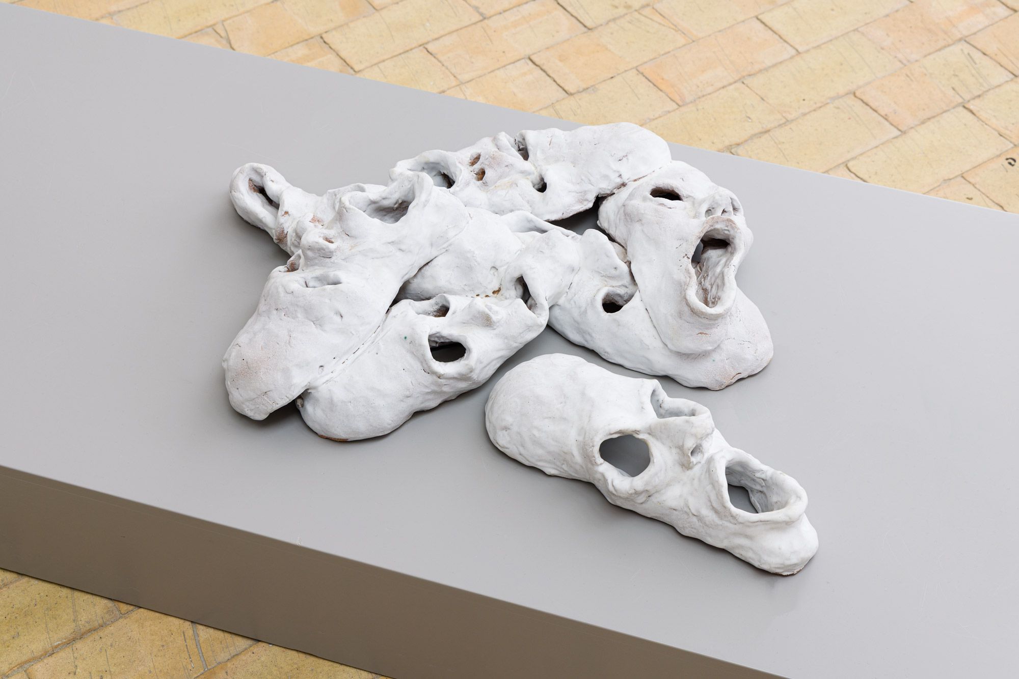 White ceramic masks with distorted facial features placed on a gray plinth.